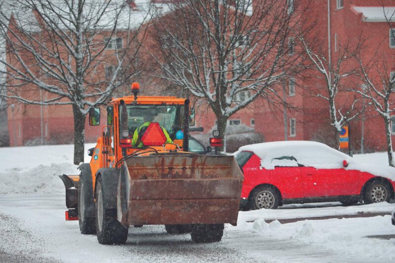 Mindre traktor som röjer snö på parkering